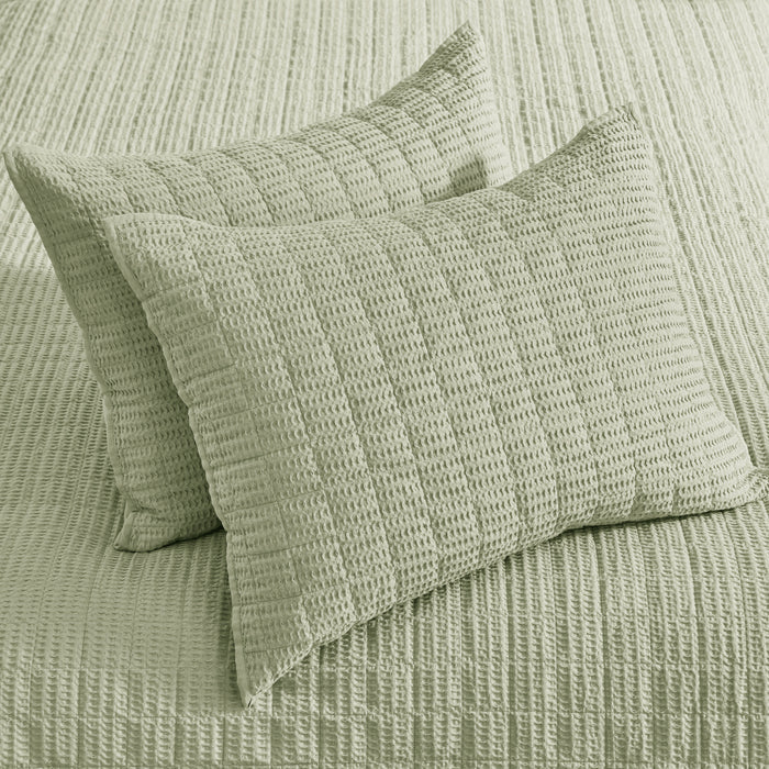 Two green textured pillows on a matching bedspread