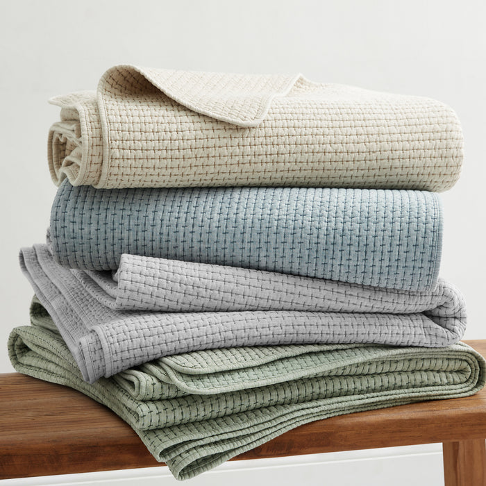 Pick-Stitch Artisan Quilted Throw stacked in neutral colors on a wooden surface, showcasing texture and comfort.