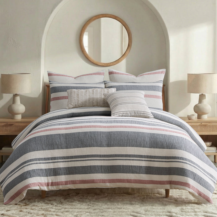 Bedroom with striped bedding, pillows, and lamps on a neutral color scheme.