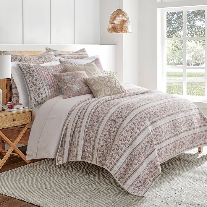 Bedroom with a bed featuring a patterned comforter and pillows, wooden nightstand, and large window.