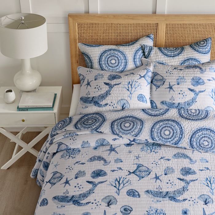 Bed with blue and white nautical patterned bedding, wooden headboard, and white nightstand.