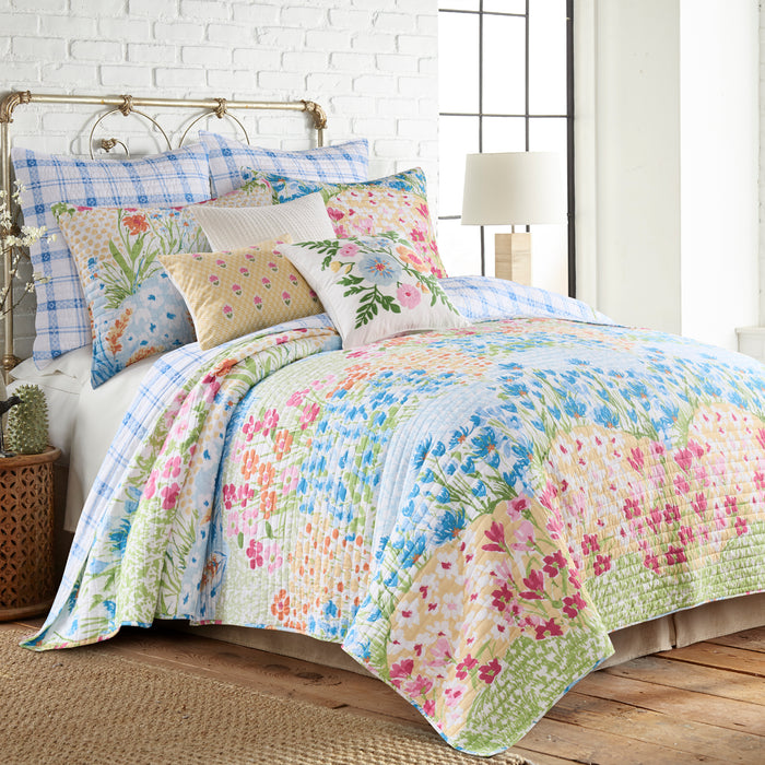 Floral quilt and pillow set on a bed in a bedroom with a white brick wall.