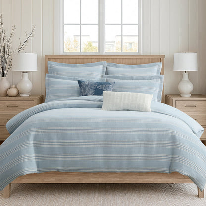 Blue striped bedding set on a bed in a bedroom with two lamps and a window.