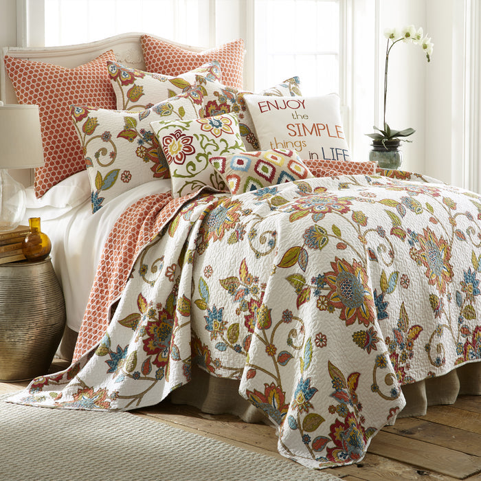 Floral quilt and pillows on a bed, pillow reads Enjoy the simple things
