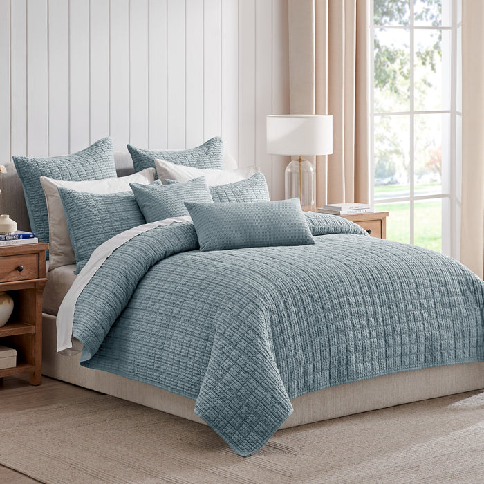 Blue textured comforter set on a bed in a bedroom with large windows.