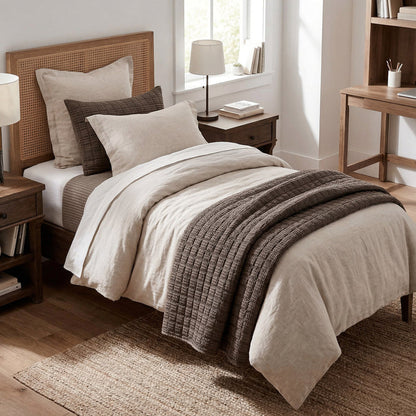 Neatly made bed with beige and brown bedding in a bedroom setting.