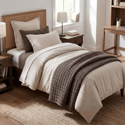 Neatly made bed with beige and brown bedding in a bedroom setting.