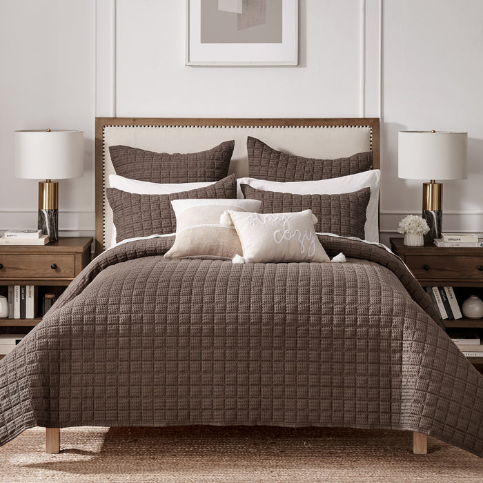 Bedroom with a brown quilted comforter on a bed, two nightstands with lamps, and a framed picture on the wall.