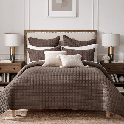 Bedroom with a brown quilted comforter on a bed, two nightstands with lamps, and a framed picture on the wall.