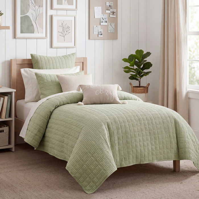 Bedroom with a bed covered in green bedding and decorative pillows.