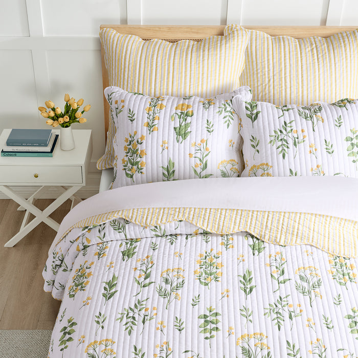 Floral bedding set on a bed with a white nightstand and flowers.