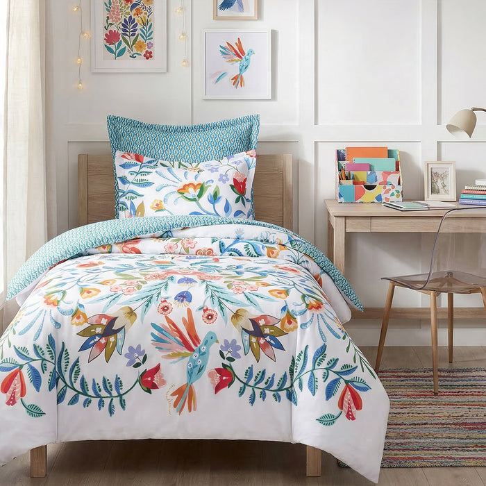 Colorful floral and bird patterned bedding set on a bed in a room with a desk and decor.