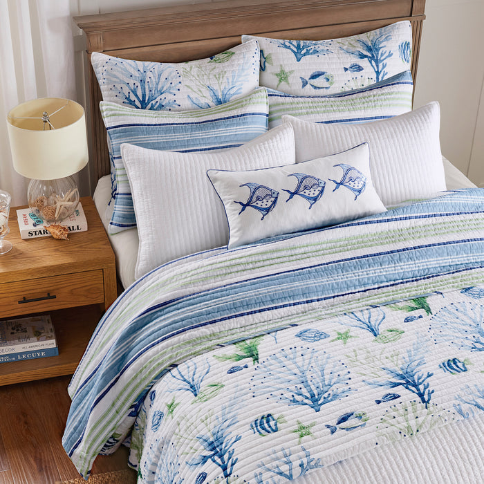 Bed with blue and white bedding featuring fish and coral patterns, next to a wooden nightstand.