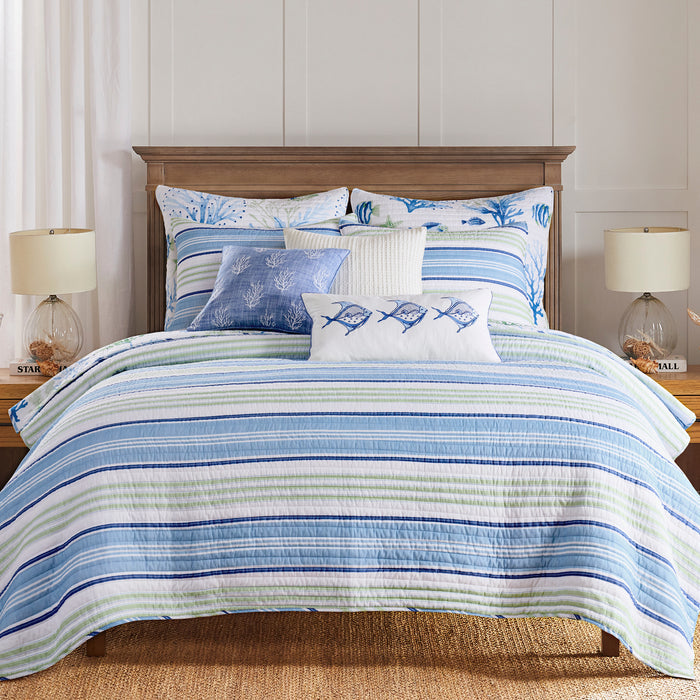 Striped bedding set on a bed with pillows and lamps in a bedroom setting.
