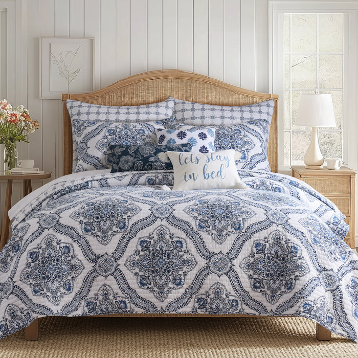 Lentana Navy Quilt Set displayed on a bed with intricate medallion pattern in navy and white, accompanied by decorative pillows.