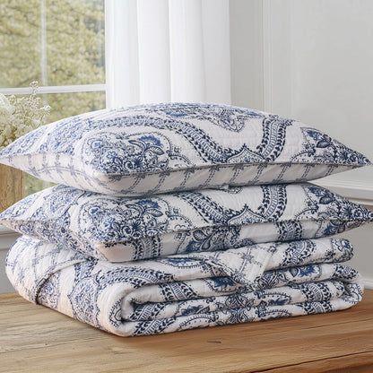 Lentana Navy Quilt Set featuring intricate medallion pattern on quilt and shams stacked on a wooden table.