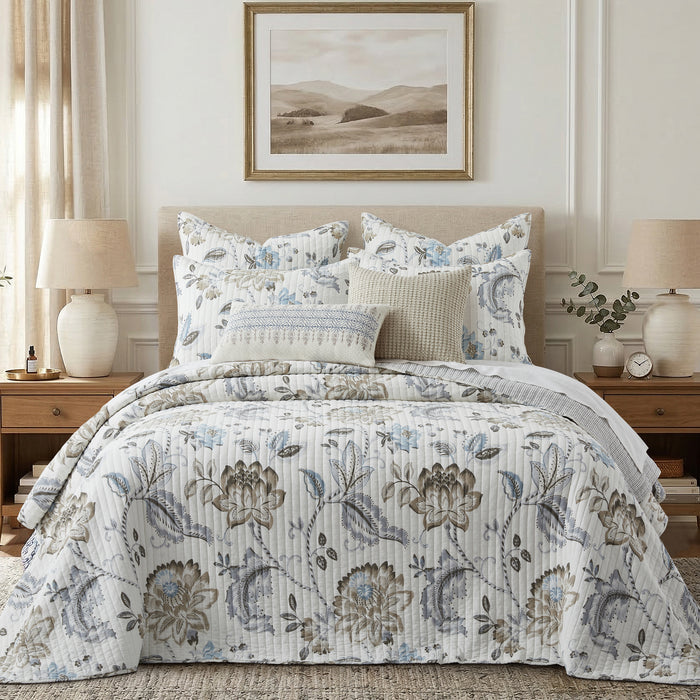 Floral patterned quilt on a bed in a bedroom setting with lamps and artwork.