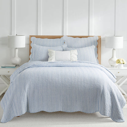 Cozy bedroom featuring a neatly made bed with light blue and white vertical striped coastal quilt set with scalloped edges and matching shams