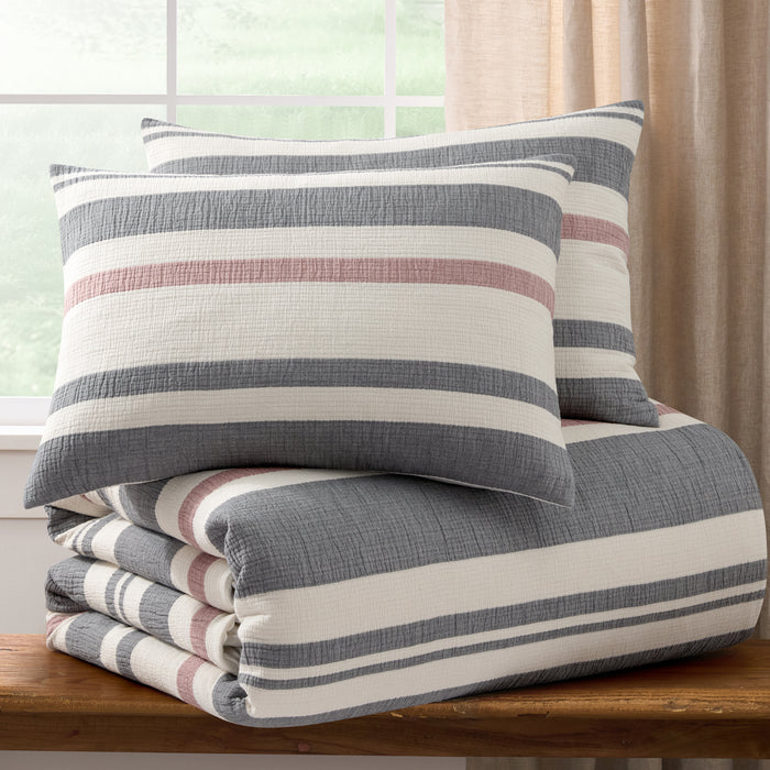 Striped pillow and blanket set on a wooden surface with a window in the background