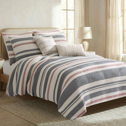 Striped bedding set on a bed in a bedroom with curtains and lamp.