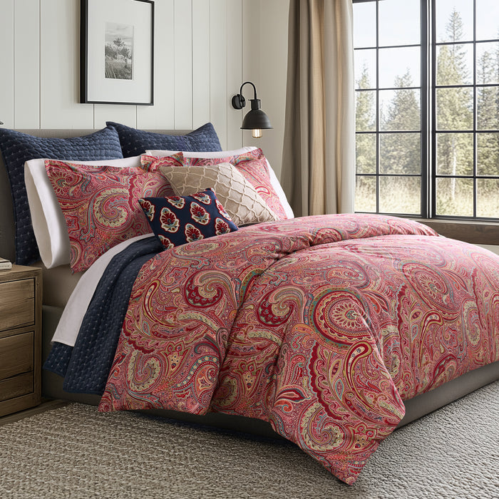 Spruce Comforter Set in vibrant paisley print featuring red and gold colors, displayed on a bed with decorative pillows.